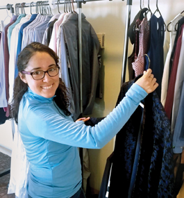 A smiling woman looks through clothes hung on racks